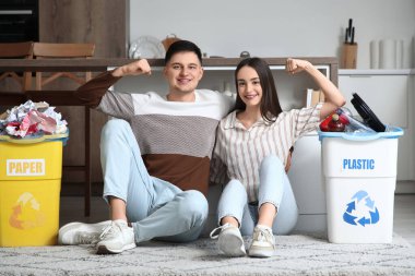 Çöpleri çöp bidonlarına dizip evde kaslarını gösteren genç bir çift. Küresel Geri Dönüşüm Günü