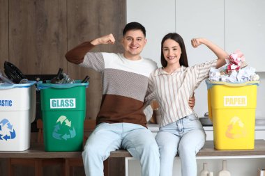 Çöpleri çöp bidonlarına dizip evde kaslarını gösteren genç bir çift. Küresel Geri Dönüşüm Günü