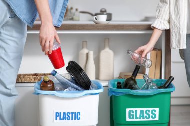 Evdeki çöp kutularında çöpleri ayıran genç bir çift, yakın çekim. Küresel Geri Dönüşüm Günü