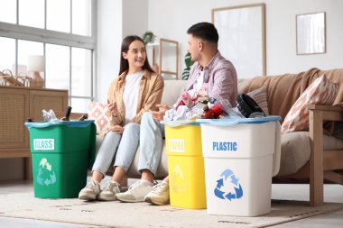 Evdeki kanepede oturan çöp bidonlarını ayıran genç bir çift. Küresel Geri Dönüşüm Günü