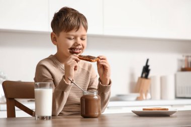 Yüzünde çikolata ezmesi olan tatlı bir çocuk mutfakta tatlı tost yiyor.