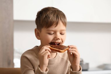 Yüzünde çikolata ezmesi olan tatlı bir çocuk mutfakta tatlı tost yiyor.