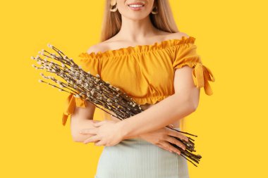 Young woman with pussy willow branches on yellow background, closeup