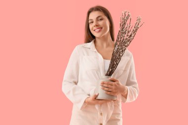 Beautiful young woman holding vase with pussy willow branches on pink background