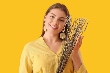 Beautiful young woman with pussy willow branches on yellow background