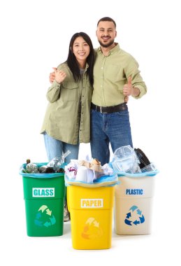 Çöp bidonlarında çöpleri ayıran genç bir çift beyaz arka planda baş parmaklarını gösteriyorlar. Küresel Geri Dönüşüm Günü