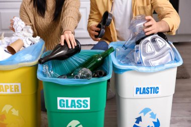 Evdeki çöp kutularında çöpleri ayıran genç bir çift, yakın çekim. Küresel Geri Dönüşüm Günü