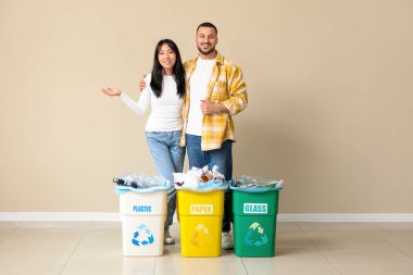 Bej duvarın yakınındaki çöp bidonlarını ayıran genç bir çift. Küresel Geri Dönüşüm Günü