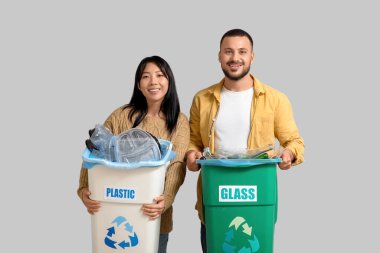 Gri arka planda çöpleri çöp kutularına ayıran genç bir çift. Küresel Geri Dönüşüm Günü