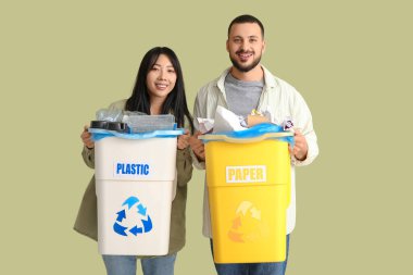 Çöpleri yeşil arka planda çöp kutularına ayıran genç bir çift. Küresel Geri Dönüşüm Günü