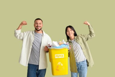 Çöpleri çöp kutusuna atıp yeşil arka planda kaslarını gösteren genç bir çift. Küresel Geri Dönüşüm Günü