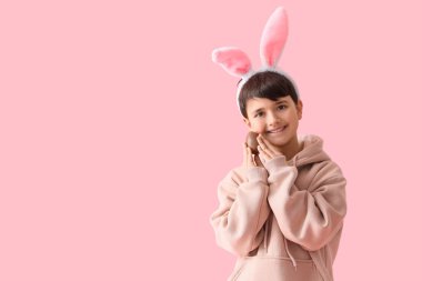 Pembe arka planda çikolata yumurtası olan tavşan kulaklı tatlı bir çocuk. Paskalya kutlaması