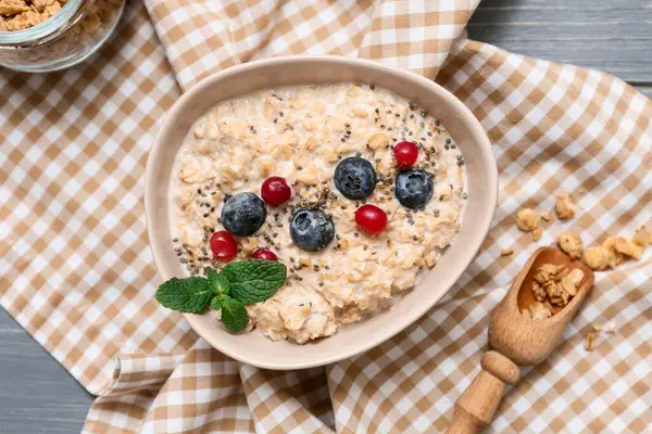 Peçete, lezzetli yulaf ezmeli kase, gri ahşap arka planda chia tohumları ve meyveler.