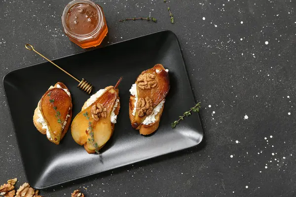 Bir tabak armut bruschetta, ricotta peyniri, ceviz ve siyah arka planda bal.