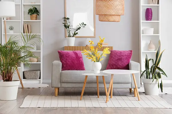 Oturma odasının içinde raflar, sehpalar ve kanepede mor yastıklar var.