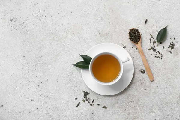 Bir fincan sıcak yeşil çay ve beyaz arka planda kurumuş yapraklı ahşap kaşık.