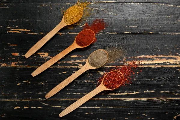 Koyu ahşap arka planda farklı aromatik baharatlı kaşıklar