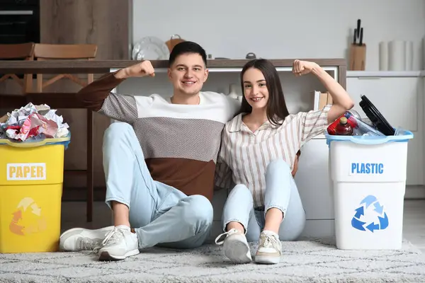 Çöpleri çöp bidonlarına dizip evde kaslarını gösteren genç bir çift. Küresel Geri Dönüşüm Günü