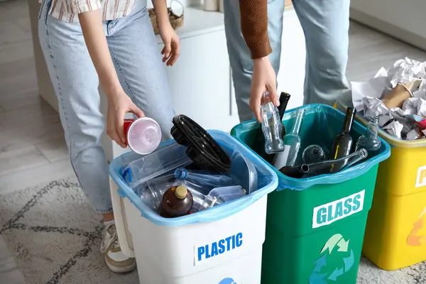 Evdeki çöp kutularında çöpleri ayıran genç bir çift, yakın çekim. Küresel Geri Dönüşüm Günü