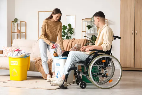 Tekerlekli sandalyedeki genç adam ve kız arkadaşı evdeki çöp kutularını düzenliyor. Küresel Geri Dönüşüm Günü
