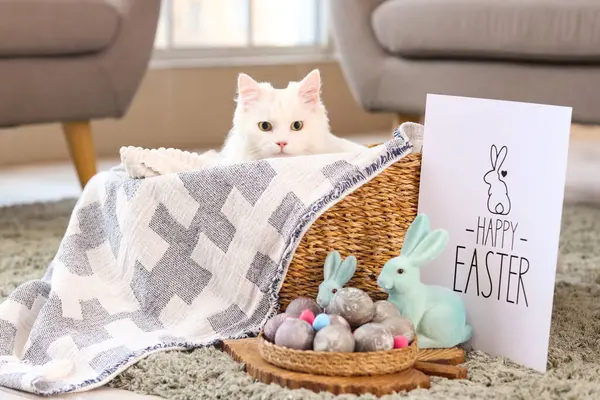 Paskalya yumurtaları, oyuncak tavşanlar ve oturma odasında tebrik kartı olan sepetteki sevimli beyaz kedi. Paskalya kutlaması