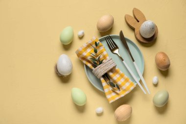 Paskalya yumurtaları ve sarı arka planda okaliptüs dallarıyla güzel bir masa.