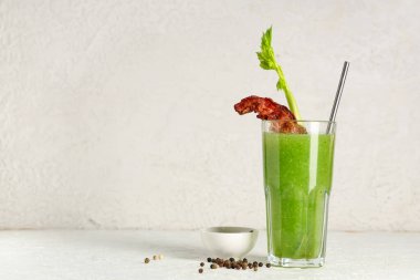 Beyaz arka planda domuz pastırması ve kerevizle süslenmiş bir bardak Bloody Mary kokteyli.