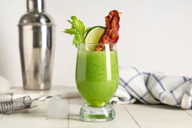 Beyaz fayans masasında pastırma, limon ve kereviz ile süslenmiş bir bardak Bloody Mary kokteyli.