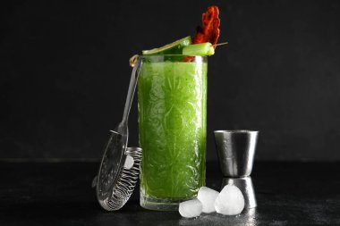 Süzgeç, buz küpleri, domuz pastırması ve kerevizle süslenmiş bir bardak Bloody Mary kokteyli.