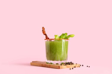 Kesme tahtası, domuz pastırması ve pembe arka planda kereviz ile süslenmiş bir bardak Bloody Mary kokteyli.