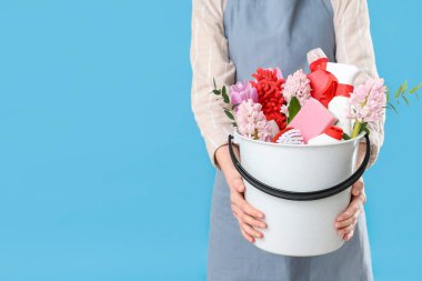 Temizlik malzemeleri ve mavi arka planda bahar çiçekleri olan kadın hademe.