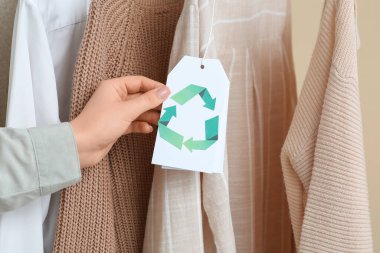 Giysilerdeki geri dönüşüm etiketini bej arka planda tutan kadın