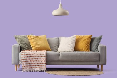 Mor arka planda yastıkları ve battaniyesi olan rahat gri kanepe.