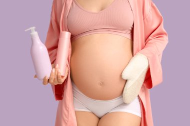 Masaj eldiveni ve mor arka planda kozmetik ürünleri olan güzel hamile kadın, yakın plan.