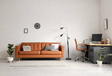 Deri koltuğu, lambası ve beyaz tuğla duvarın yanındaki işyeri olan modern ofis.