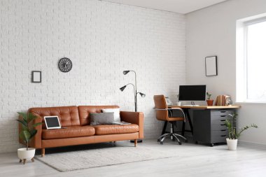 Deri koltuğu, lambası ve beyaz tuğla duvarın yanındaki işyeri olan modern ofis.