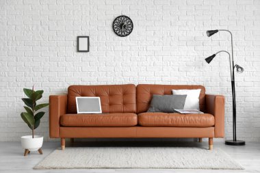 Beyaz tuğla duvarın yanındaki deri koltukta lamba, çiçek ve dizüstü bilgisayarlı modern ofis.