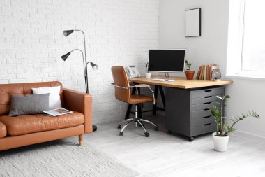 Deri koltuğu, lambası ve beyaz tuğla duvarın yanındaki işyeri olan modern ofis.
