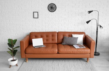 Beyaz tuğla duvarın yanındaki deri koltukta lamba, çiçek ve dizüstü bilgisayarlı modern ofis.