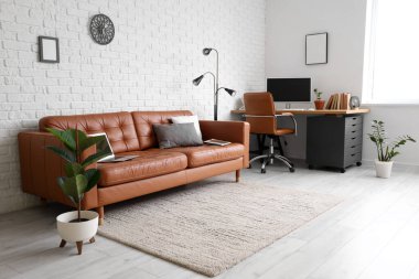 Deri koltuğu, lambası ve beyaz tuğla duvarın yanındaki işyeri olan modern ofis.