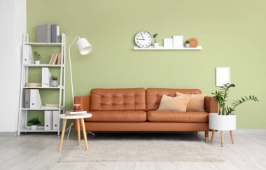 Deri kanepesi, sehpası ve yeşil duvarın yanında raf ünitesi olan modern ofis.