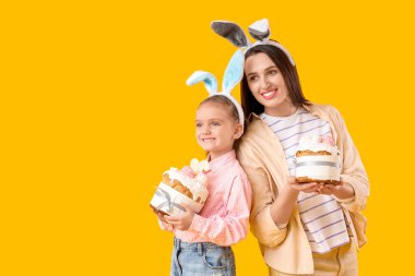 Güzel genç bir kadın ve sarı arka planda Paskalya pastaları olan tavşan kulaklı küçük tatlı kızı.