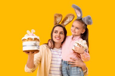 Güzel genç bir kadın ve sarı arka planda Paskalya pastaları olan tavşan kulaklı küçük tatlı kızı.