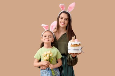 Paskalya pastası ve kahverengi arka planda lale çiçekleri tutan sevimli küçük kızı ile tavşan kulaklı güzel genç bir kadın.