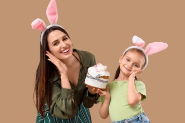 Güzel genç bir kadın ve küçük tatlı kızı tavşan kulaklı ve kahverengi arka planda Paskalya pastası