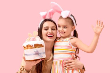 Paskalya pastası ve pembe arka planda tavşan kulaklı küçük tatlı kızı olan güzel genç bir kadın.