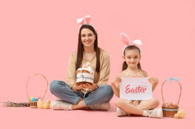 Paskalya pastası, tebrik kartı ve pembe arka planda oturan piliçlerle güzel, genç bir kadın ve tavşan kulaklı tatlı kızı.
