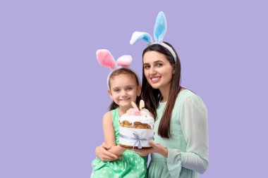 Güzel genç bir kadın ve küçük tatlı kızı tavşan kulaklı Paskalya pastası ve leylak arka planda