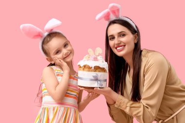 Güzel genç bir kadın ve pembe arka planda Paskalya pastası olan tavşan kulaklı küçük tatlı kızı.