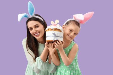 Güzel genç bir kadın ve küçük tatlı kızı tavşan kulaklı Paskalya pastası ve leylak arka planda